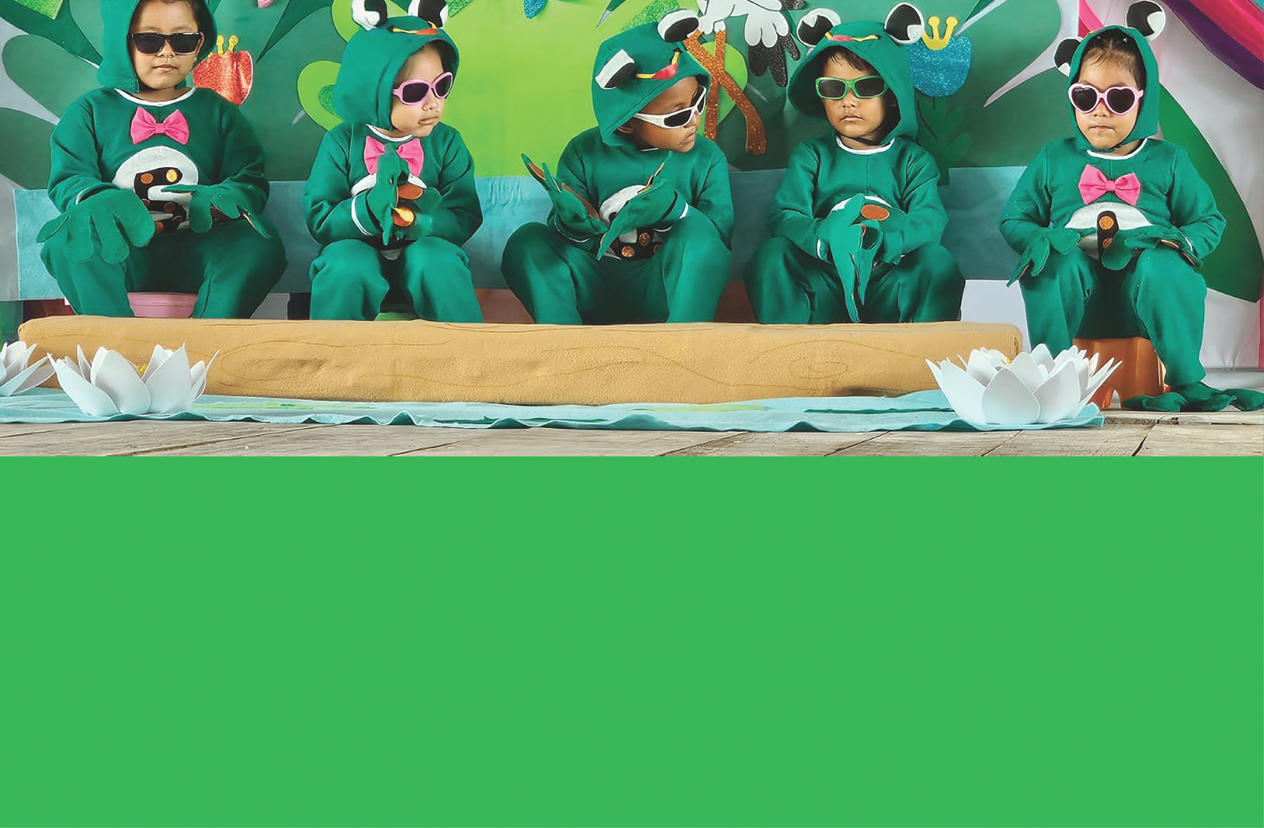 A group of children in green costumes sitting on a mat. Description generated by AI