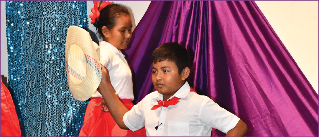 Two children wearing white and red dresses are on a stage. Description generated by AI